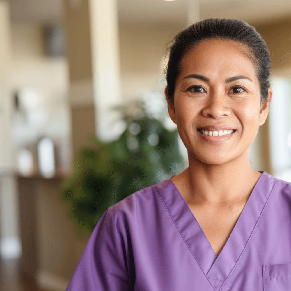 Nurse in scrubs smiling at camera with hospital or care facility in background